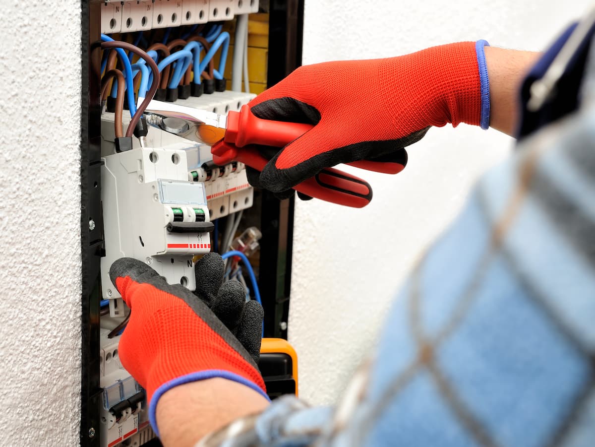 Trabajador con guantes de seguridad manipulando un panel eléctrico, equipo de Ferreterías Guevara