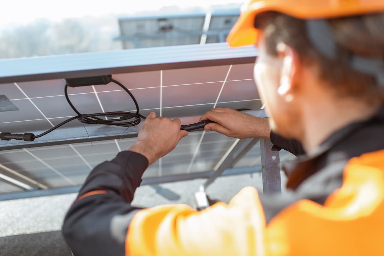 Técnico instalando un sistema de energía solar, conectando cables bajo un panel solar, demostrando la eficiencia de los productos de Ferreterías Guevara