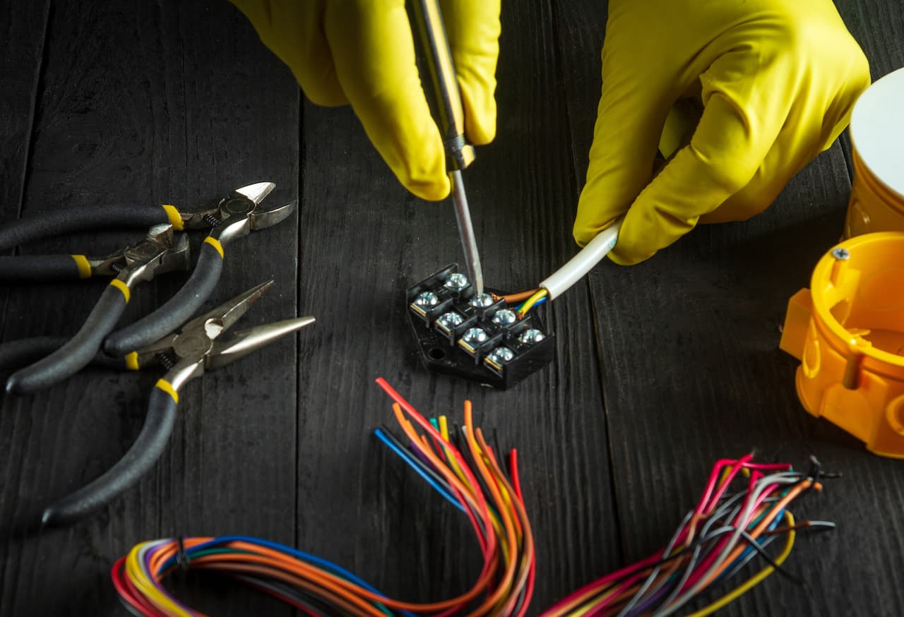 Manos con guantes amarillos ajustando cables eléctricos, equipo de Ferreterías Guevara