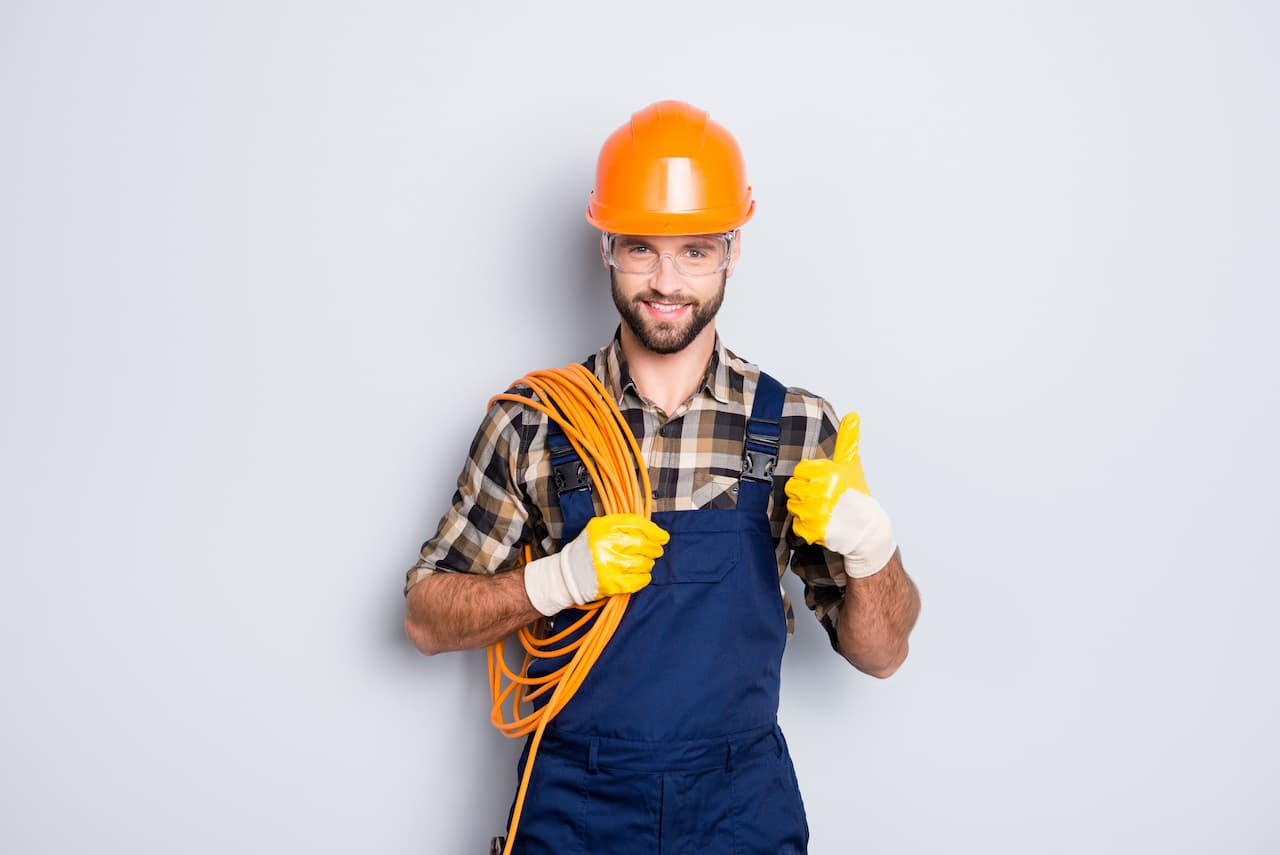 Electricista con casco y guantes, sosteniendo un rollo de cable y mostrando un pulgar arriba, reflejando la calidad de los productos de Ferreterías Guevara