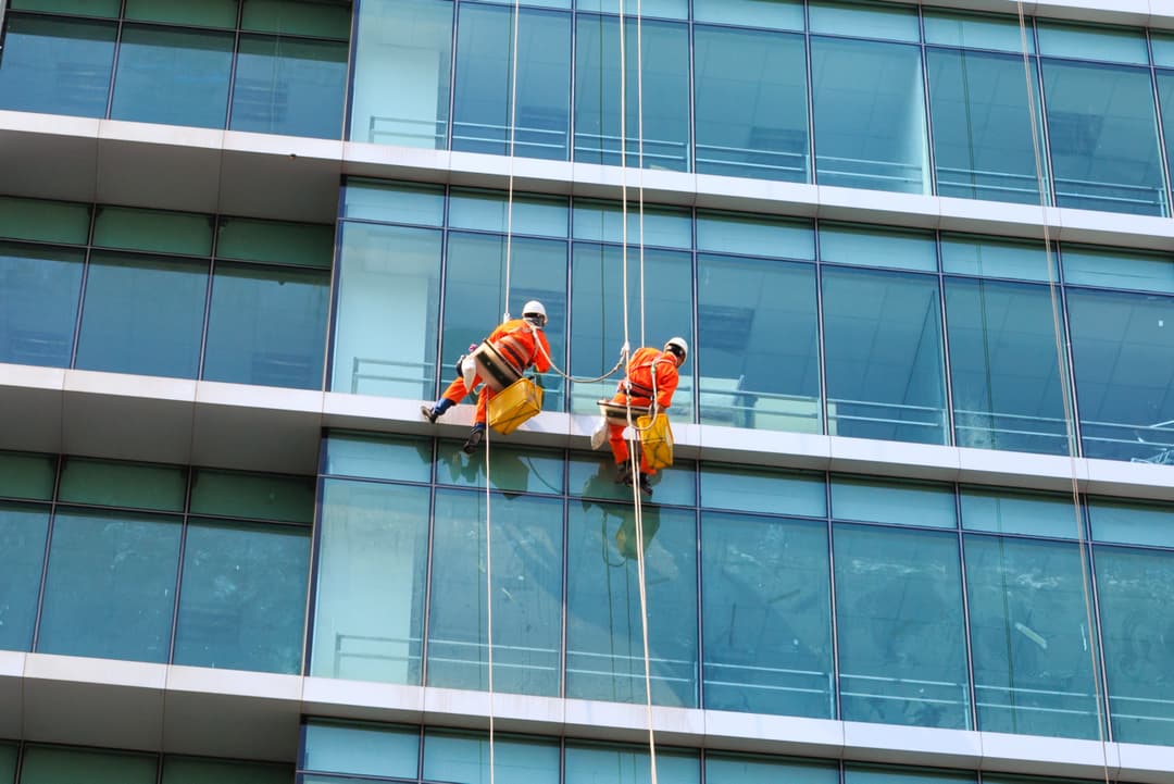 Personal de limpieza de ventanas en rascacielos utilizando equipo especializado de Ferreterías Guevara