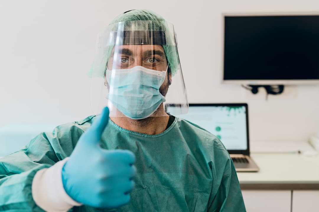 Investigador en laboratorio médico dando un pulgar hacia arriba, usando equipo de protección de Ferreterías Guevara