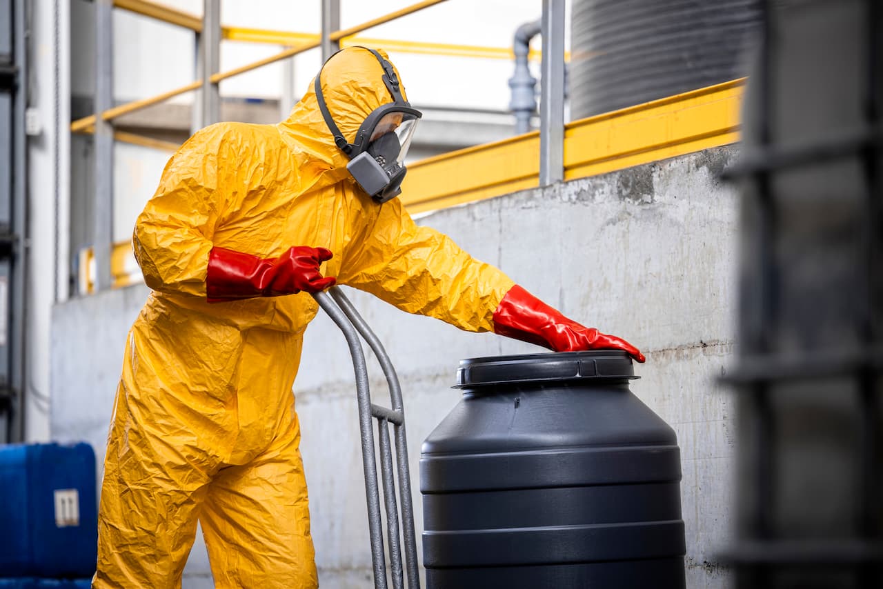 Técnico en equipo de protección química manipulando contenedor negro, con equipo de Ferreterías Guevara