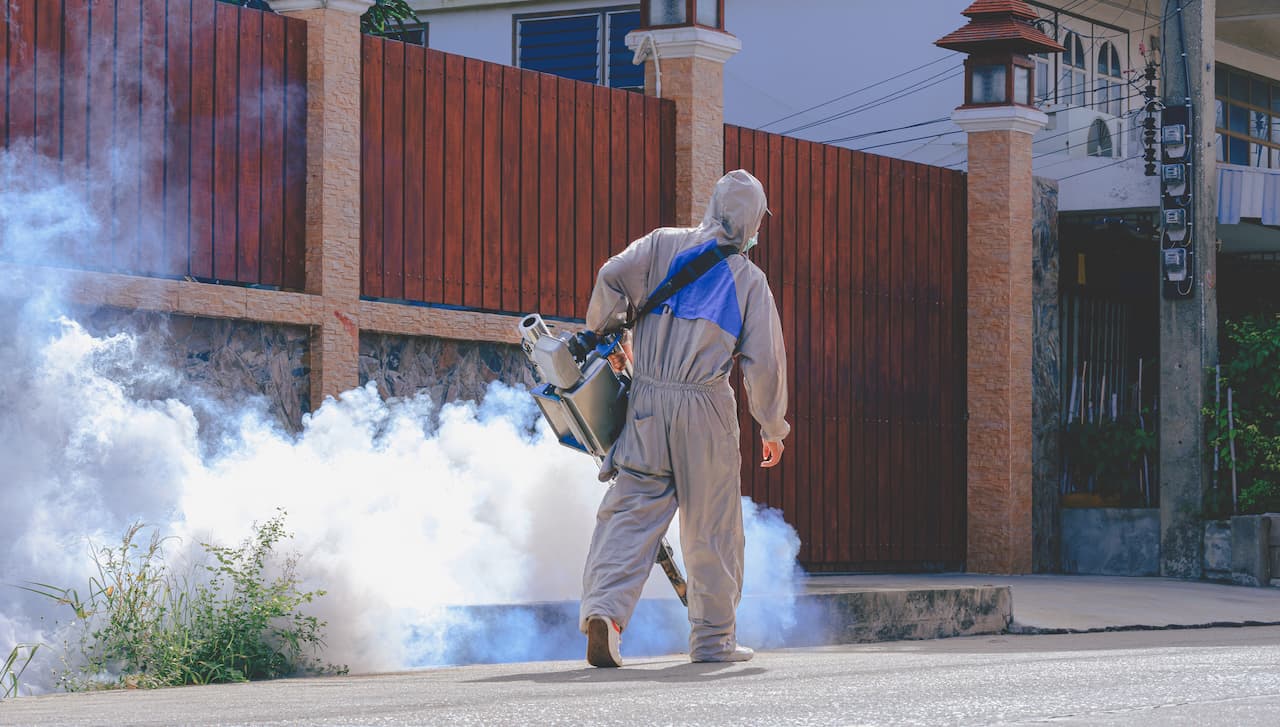 Trabajador con equipo de protección fumigando una área al aire libre
