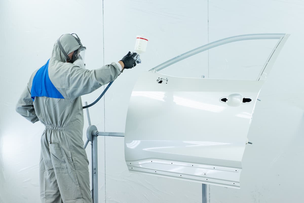 Trabajador pintando la puerta de un automóvil con equipo de protección de Ferreterías Guevara