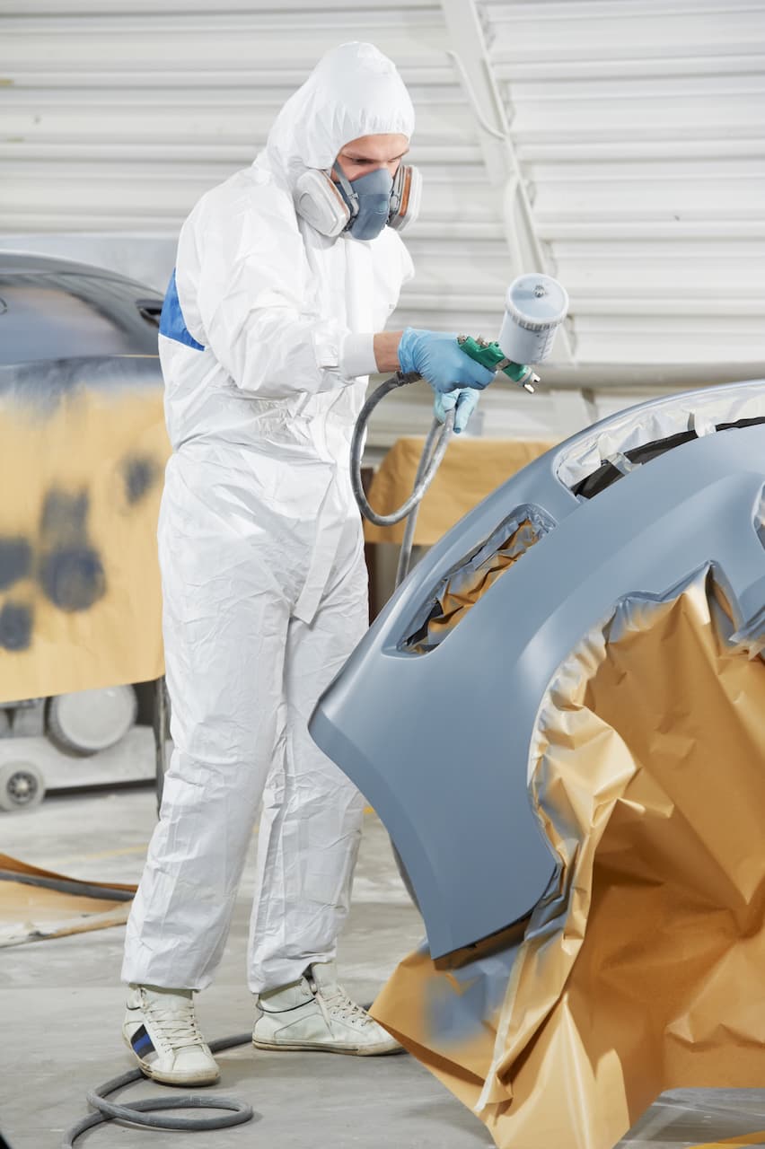 Trabajador pintando un automóvil con equipo de protección de Ferreterías Guevara, incluyendo mascarilla y mono desechable